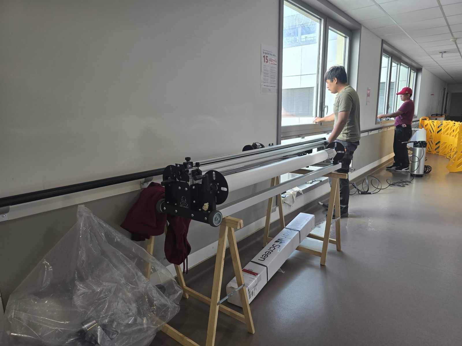 Rouleau de film solaire Solar Screen 70 C monté sur son dérouleur dans un couloir de la Clinique Saint-Jean l'Ermitage, techniciens DFP France au travail sur les fenêtres