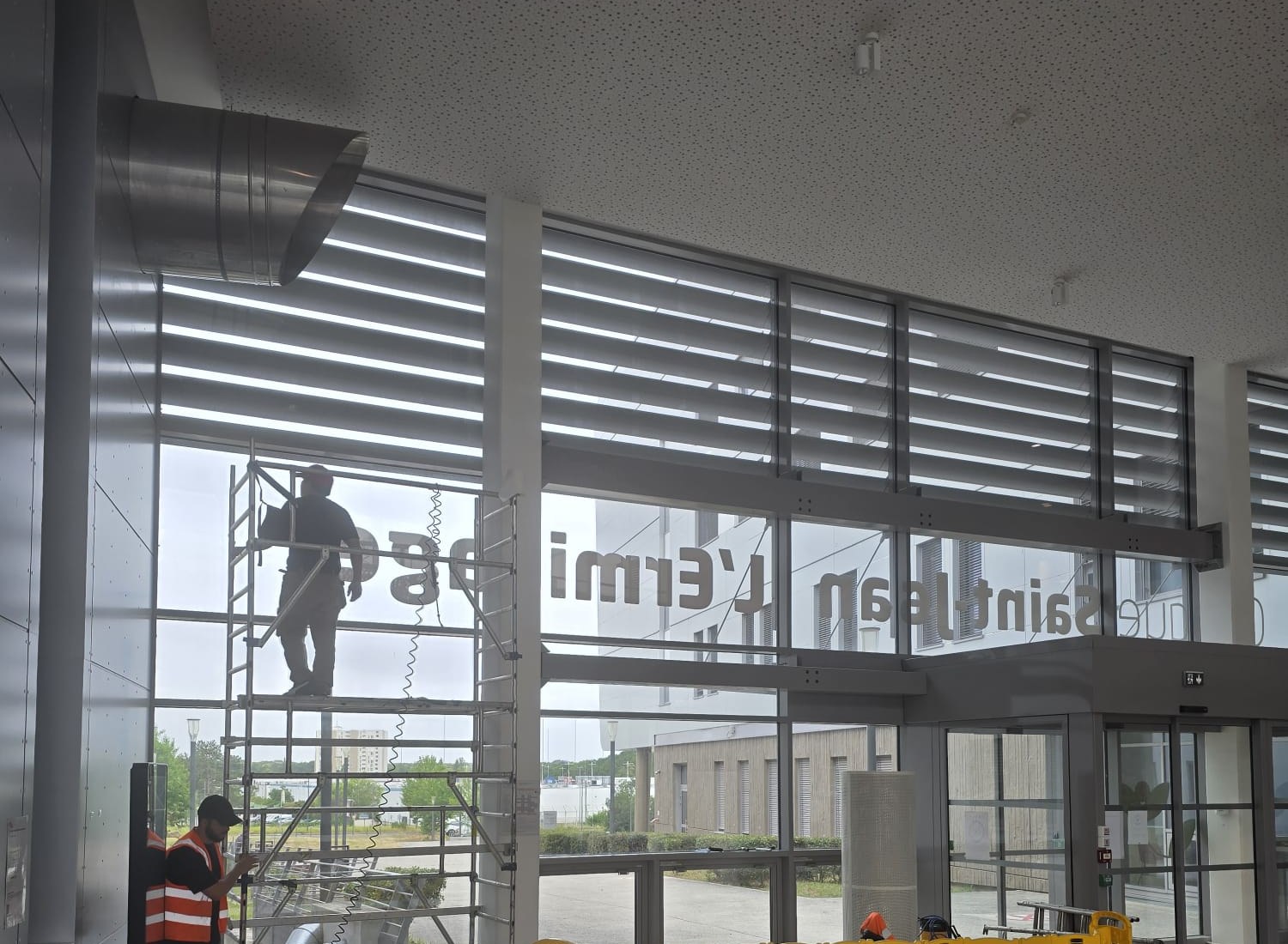 Technicien DFP France posant le film solaire sur la façade vitrée toute hauteur du hall de la Clinique Saint-Jean l'Ermitage à Melun (77), depuis un échafaudage