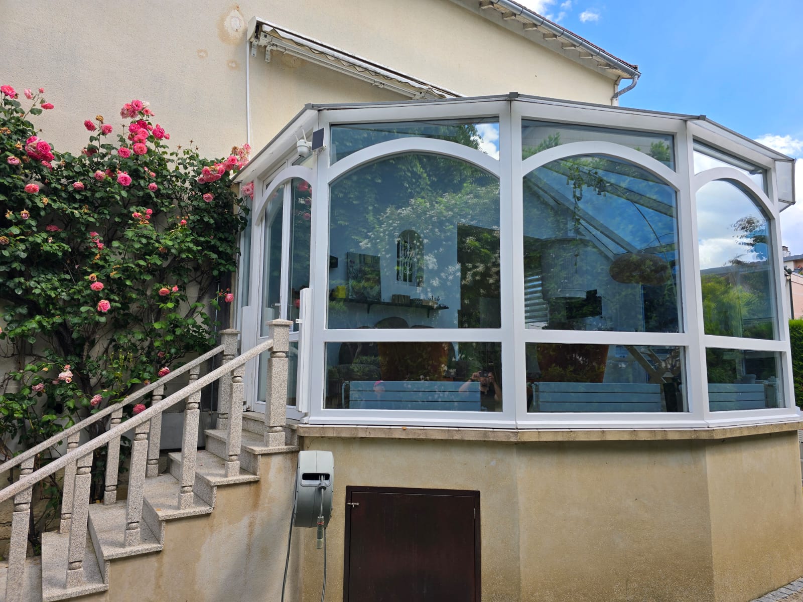 Véranda d'une maison en Île-de-France après pose de film solaire par DFP France — vitrages réfléchissants renvoyant le ciel bleu, surchauffe stoppée