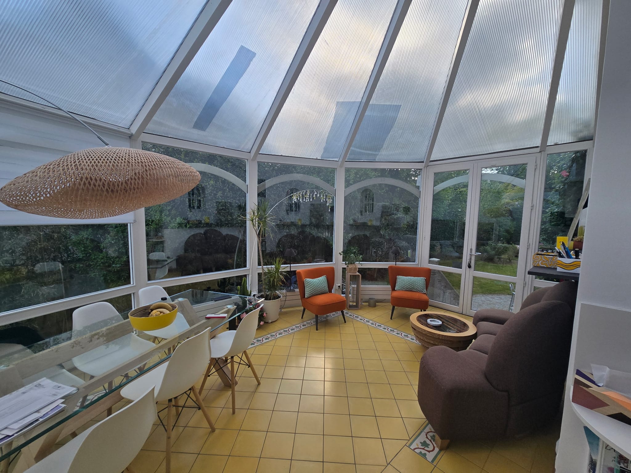 Véranda avant pose de film solaire — vitrages transparents sous un ciel gris, on voit directement à l'intérieur, maison en Île-de-France