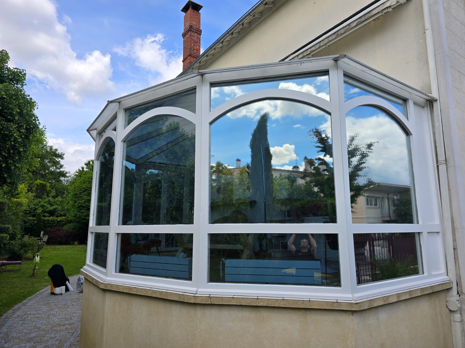 Vue extérieure d'ensemble de la véranda après traitement — vitrages réfléchissants renvoyant le ciel bleu, façade résidentielle en Île-de-France