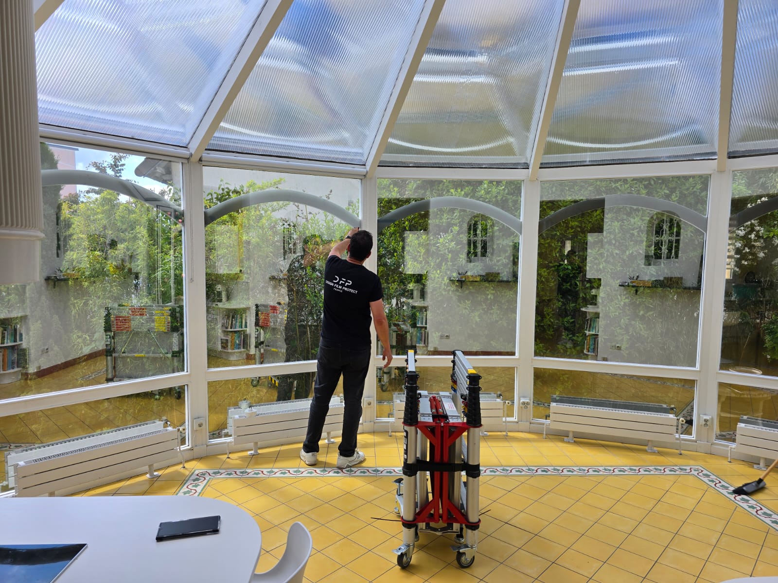 Technicien DFP France en pleine pose du film solaire sur la toiture vitrée de la véranda, depuis l'intérieur
