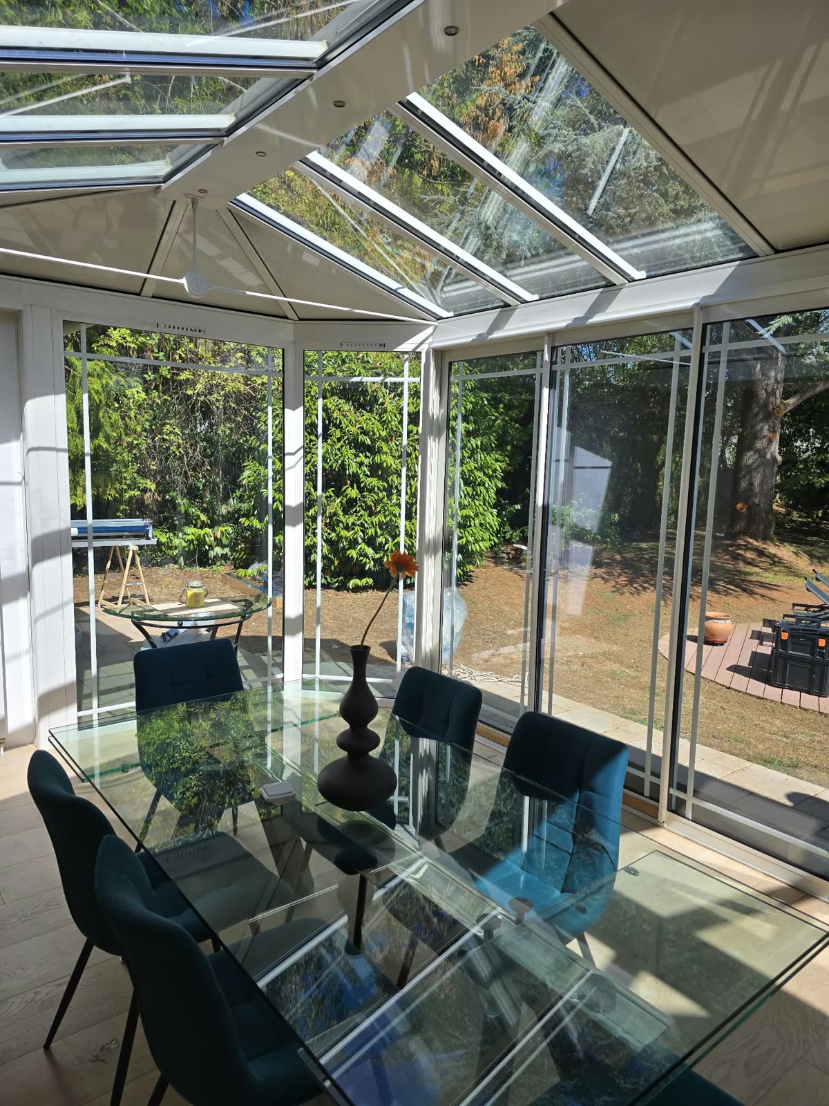Intérieur de la véranda à Lésigny après pose du film solaire : table à manger sous la toiture vitrée, lumière naturelle conservée
